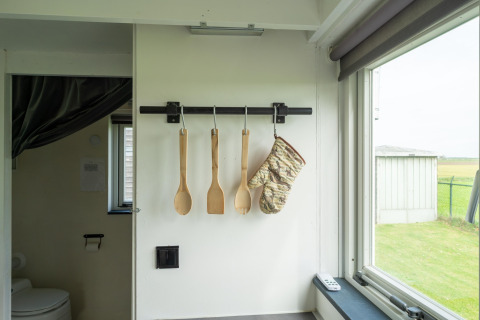 Utensilios de cocina y un guante de horno colgados en una Tiny House en Países Bajos, con ventana.