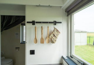 Utensilios de cocina y un guante de horno colgados en una Tiny House en Países Bajos, con ventana.