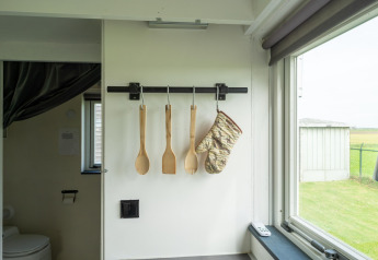 Ustensiles de cuisine et gant de four accrochés dans un Tiny House aux Pays-Bas avec vue sur fenêtre.