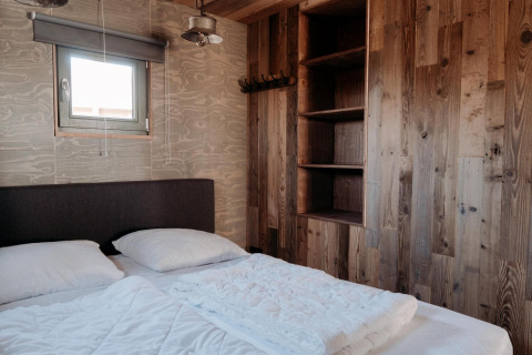 Camera da letto al Juttershut Duynpark - Callantsoog, Paesi Bassi, con pareti in legno, letto e finestra.