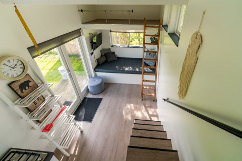 Licht en modern interieurtje van een tiny house in Nederland met trap, slaaploft en gezellige zithoek.