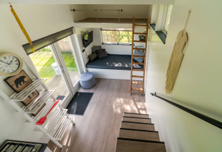 Licht en modern interieurtje van een tiny house in Nederland met trap, slaaploft en gezellige zithoek.