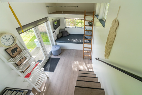 Licht en modern interieurtje van een tiny house in Nederland met trap, slaaploft en gezellige zithoek.