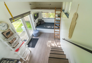 Interior de tiny house luminosa y moderna en Países Bajos, con altillo, escaleras y zona de estar confortable.