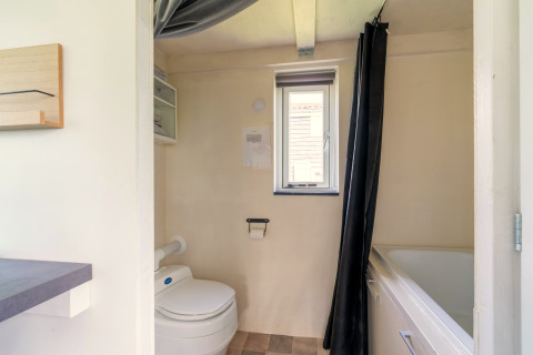 Badkamer van een tiny house in Nederland met toilet, bad, raam en lichte muren.