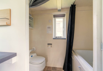 Badkamer van een tiny house in Nederland met toilet, bad, raam en lichte muren.