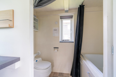 Baño en una tiny house en los Países Bajos con inodoro, bañera, ventana y paredes claras.