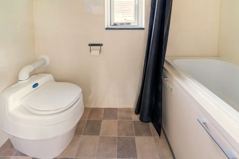 Badkamer in een tiny house in Nederland met modern toilet, bad, betegelde vloer en klein raam.