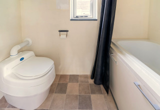 Badkamer in een tiny house in Nederland met modern toilet, bad, betegelde vloer en klein raam.