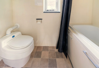 Badkamer in een tiny house in Nederland met modern toilet, bad, betegelde vloer en klein raam.