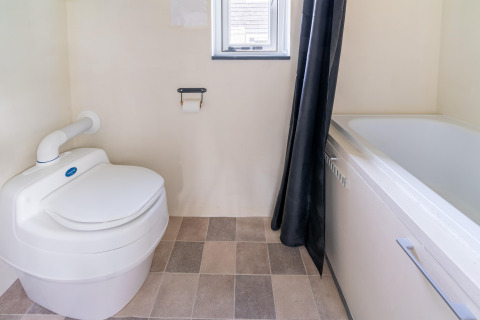 Baño en una tiny house en Países Bajos, con inodoro moderno, bañera, ventana pequeña y suelo de baldosas.