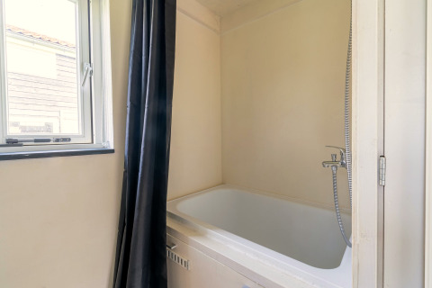 Moderne kleine badkamer met ligbad, douchegordijn en raam in een tiny house in Nederland.