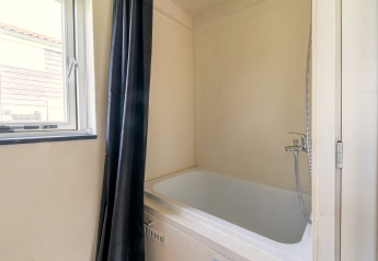Moderne kleine badkamer met ligbad, douchegordijn en raam in een tiny house in Nederland.