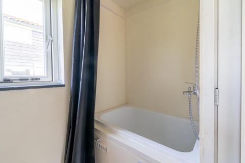 Baño pequeño y moderno con bañera, cortina negra y ventana en una tiny house de los Países Bajos.