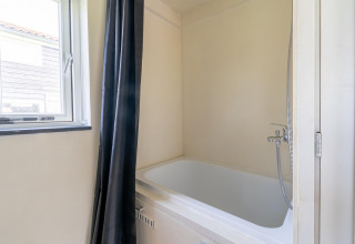 Baño pequeño y moderno con bañera, cortina negra y ventana en una tiny house de los Países Bajos.