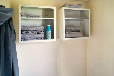 Twee wandkasten met opgevouwen grijze handdoeken en een fles poetsmiddel in een tiny house badkamer.