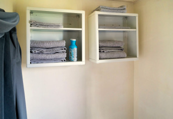 Twee wandkasten met opgevouwen grijze handdoeken en een fles poetsmiddel in een tiny house badkamer.