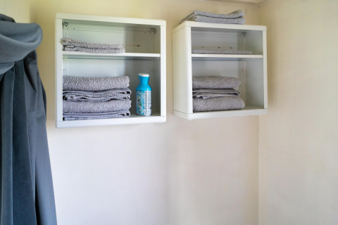 Dos estantes de pared con toallas grises dobladas y una botella de limpieza en un baño de tiny house.