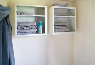 Dos estantes de pared con toallas grises dobladas y una botella de limpieza en un baño de tiny house.