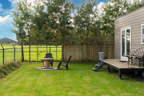 Groene tuin met stoelen en tafel naast een tiny house in Nederland, zicht op velden en bomen.