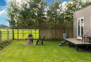 Groene tuin met stoelen en tafel naast een tiny house in Nederland, zicht op velden en bomen.