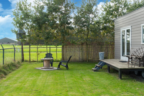 Jardín verde con dos sillas y mesa junto a una tiny house en Países Bajos, rodeado de campo y árboles.