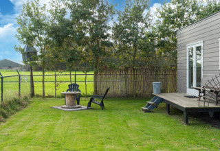 Jardín verde con dos sillas y mesa junto a una tiny house en Países Bajos, rodeado de campo y árboles.
