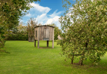 Klein houten huisje op poten in een groene tuin met bomen, gefotografeerd bij Tiny House in Nederland.