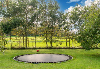 Grasveld met ingegraven trampoline en rode bal, omringd door bomen en hekwerk in Nederland.