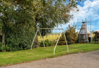 Jardin avec balançoire, pelouse et vue rurale à Tiny House aux Pays-Bas sous ciel bleu.