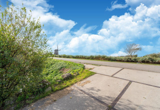 Paisaje con carretera, molino de viento y árboles cerca de Tiny House en los Países Bajos bajo cielo azul.