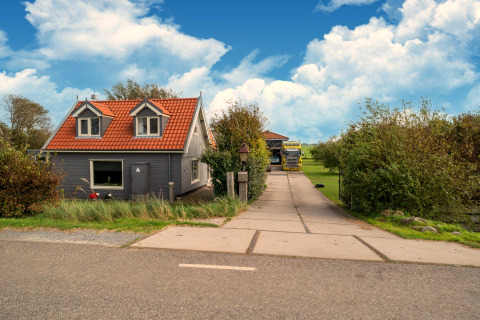 Tiny house met rood dak en grijze gevel, oprit en tuingroen onder blauwe hemel in Nederland.