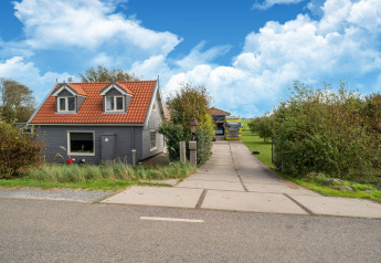 Tiny house avec toit rouge, façade grise, allée et jardin verdoyant sous ciel bleu aux Pays-Bas.