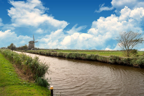 Mooie blik op een kanaal, groene velden en een windmolen bij een Tiny House in Nederland.
