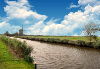 Mooie blik op een kanaal, groene velden en een windmolen bij een Tiny House in Nederland.