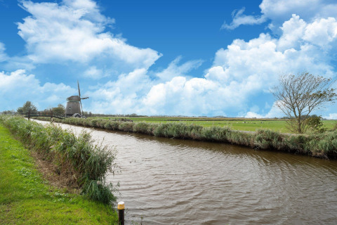 Hermosa vista de un canal, prados verdes y un molino holandés en una Tiny House en los Países Bajos.