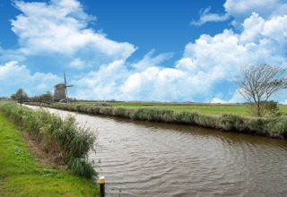 Hermosa vista de un canal, prados verdes y un molino holandés en una Tiny House en los Países Bajos.