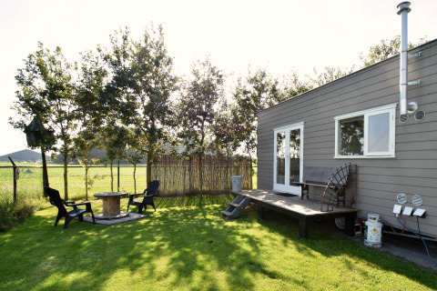 Kleine woning met terras en tuin, zitplaats in de zon, gelegen in een weide in Nederland.