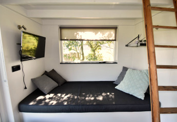 Gezellig interieur van tiny house in Nederland met bed, kussens, tv, raam en houten ladder.