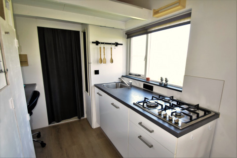 Moderne keuken in een tiny house in Nederland met gaskookplaat, spoelbak en groot raam met uitzicht.