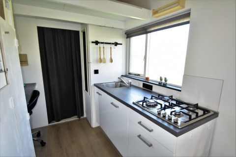 Cocina moderna en una tiny house en los Países Bajos, con estufa de gas, fregadero y ventana grande.