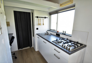 Cocina moderna en una tiny house en los Países Bajos, con estufa de gas, fregadero y ventana grande.