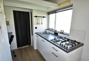Cuisine moderne d’une tiny house aux Pays-Bas, équipée d’une gazinière, évier et grande fenêtre.