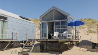 Modern strandhuis op Resort Beach Houses Julianadorp 1 met terrasstoelen en blauwe parasol op het zandstrand.