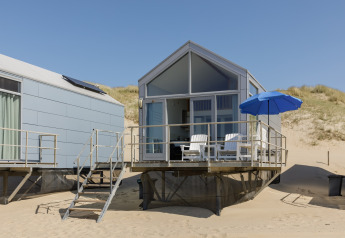 Modern strandhuis op Resort Beach Houses Julianadorp 1 met terrasstoelen en blauwe parasol op het zandstrand.