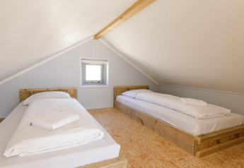 Zolderkamer met twee eenpersoonsbedden op houten frames in Beach Houses Julianadorp 1, Nederland.