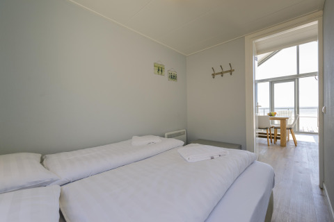 Camera da letto con due letti singoli, lenzuola bianche e vista sulla zona pranzo al Beach Houses Julianadorp.