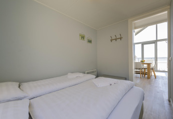 Slaapkamer met twee eenpersoonsbedden, wit beddengoed en zicht op eethoek bij Beach Houses Julianadorp.