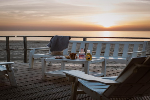 Tramonto al Resort Beach Houses Julianadorp 1 nei Paesi Bassi con sedie bianche, tavolo e bevande.