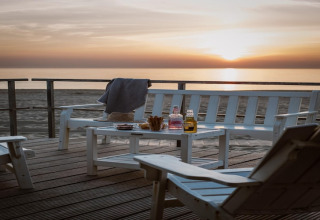Tramonto al Resort Beach Houses Julianadorp 1 nei Paesi Bassi con sedie bianche, tavolo e bevande.